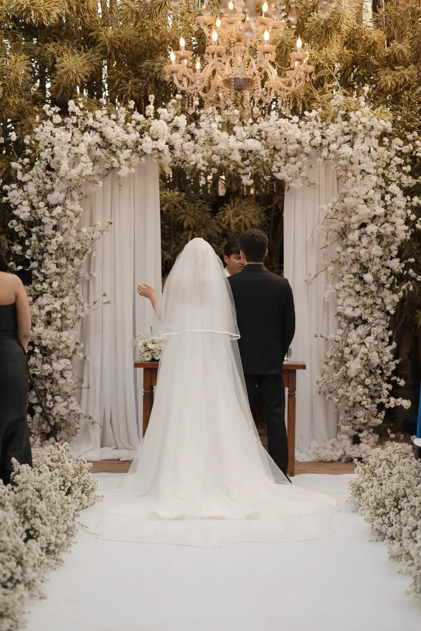 A noiva de costas no altar, o véu longo caído sobre a cauda do vestido.