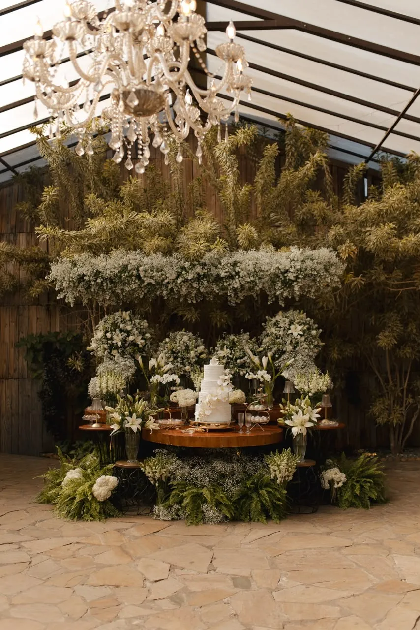 A mesa do bolo montada sob a cobertura de vidro, com o jardim atrás.