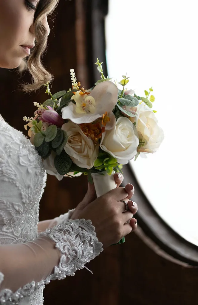 Detalhe do buquê de rosas claras contra o vestido de renda.