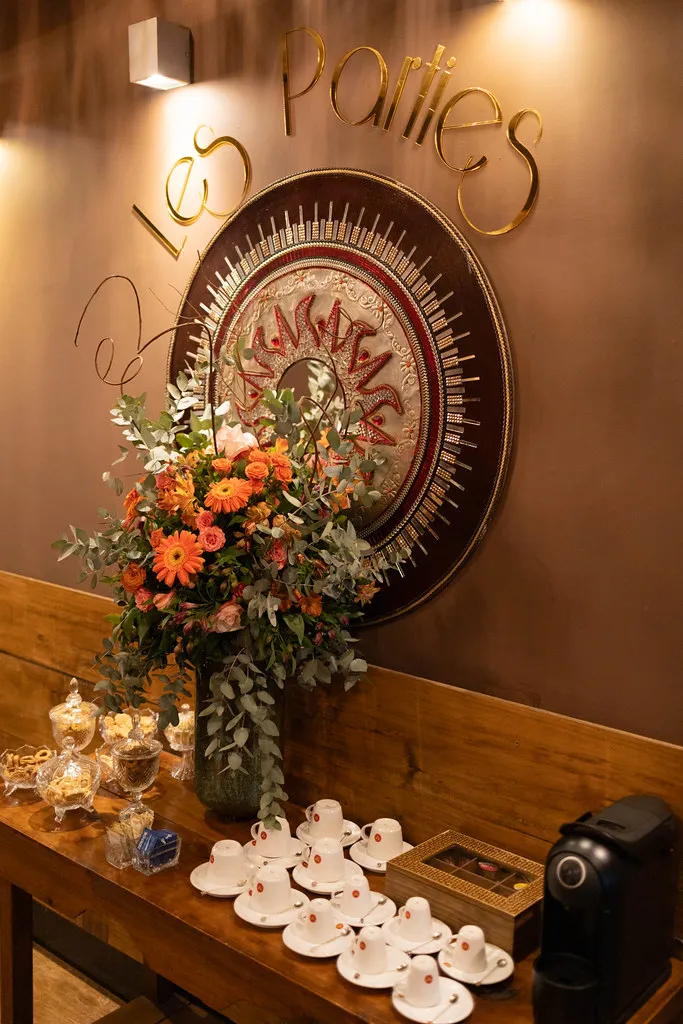 O medalhão Les Parties na parede, com o arranjo de flores à frente.